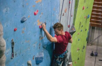 male rock climber in red shirt along blue rock wall face in gym