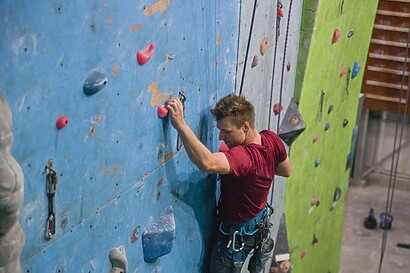 male rock climber in red shirt along blue rock wall face in gym