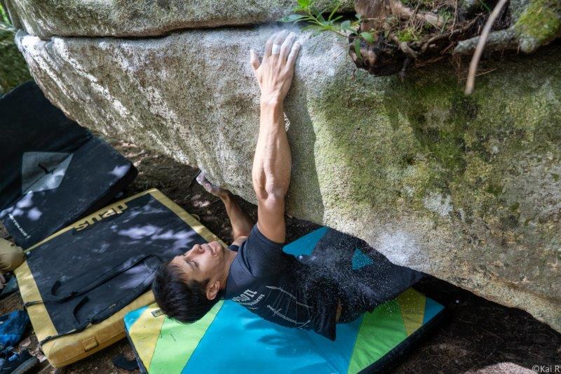 man rock climbing upside down shot with colourful crash pad